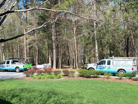 Two power washing trucks cleaning a driveway at a large home.